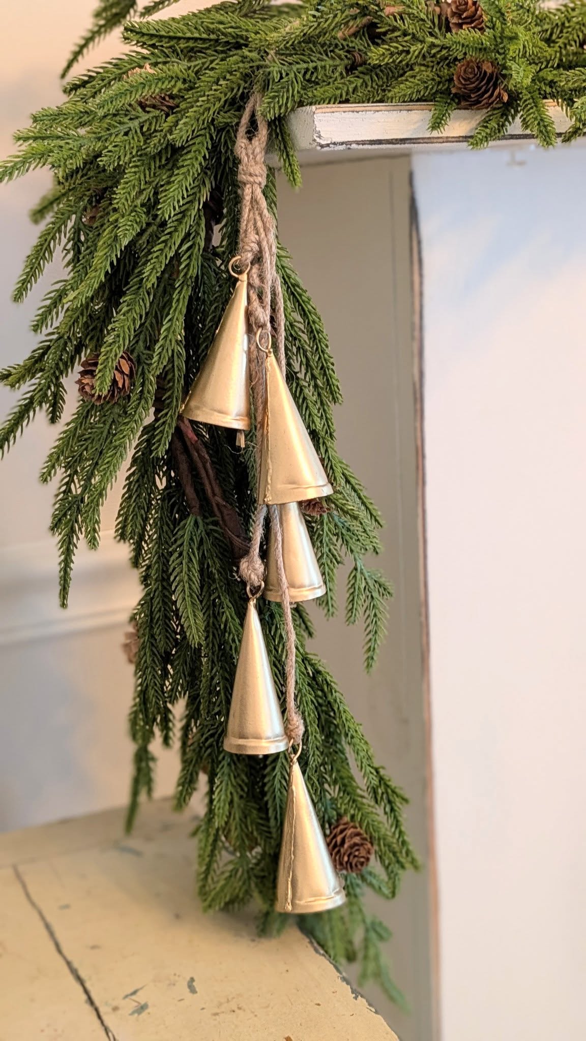 Decorative hanging with greenery and gold bells on a white surface.