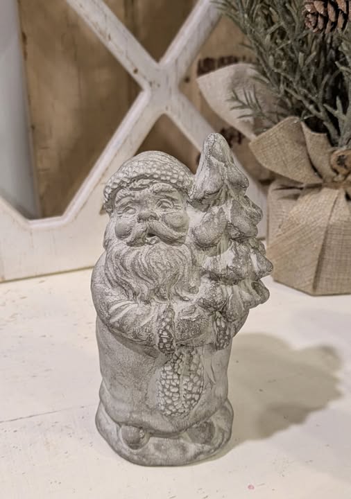 Decorative stone Santa Claus figure holding a tree on a light wooden surface.